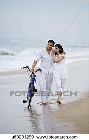 Stock Photo - Couple walking on a beach with a bicycle . Fotosearch
