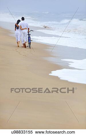 Couple walking on a beach with a bicycle View Large Photo Image Stock Photography - Couple walking on a beach with a bicycle . Fotosearch