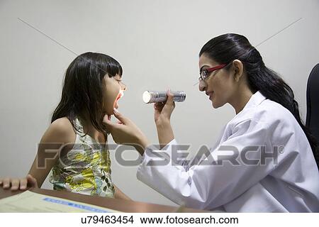 Picture - Doctor looking inside a girls mouth with a torch . Fotosearch