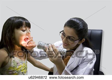 Stock Image - Doctor looking inside a girls mouth with a torch . Fotosearch