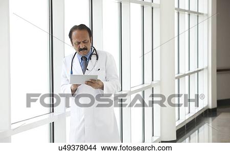Doctor reading a report on a digital tablet View Large Photo Image Picture - Doctor reading a report on a digital tablet. Fotosearch