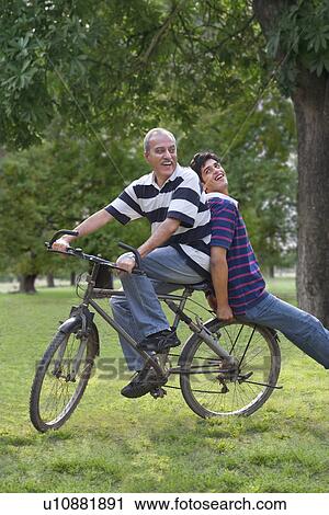 Stock Image - Father riding a bicycle while son sits behind . Fotosearch