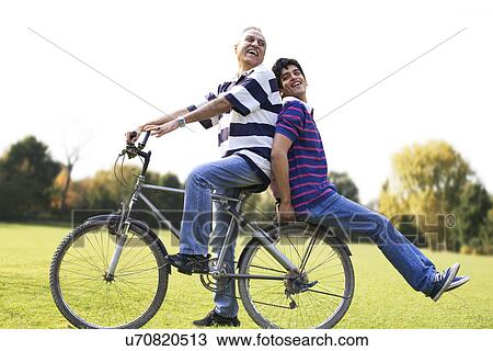 Stock Image - Father riding a bicycle while son sits behind . Fotosearch