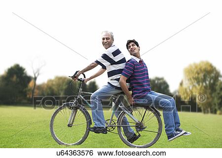 Father riding a bicycle while son sits behind View Large Photo Image Stock Photograph - Father riding a bicycle while son sits behind . Fotosearch
