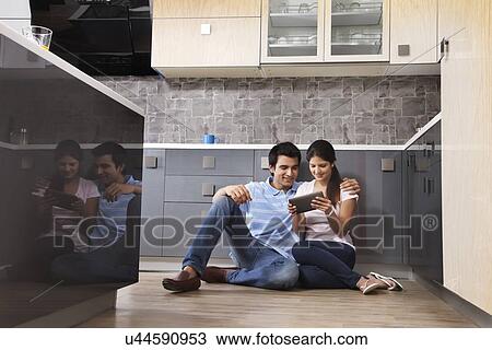 Stock Image - Full length of couple using digital tablet in kitchen. Fotosearch