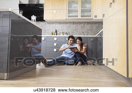 Stock Photo - Full length of Indian couple using digital tablet in kitchen. Fotosearch