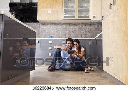 Stock Photography - Full length of Indian couple using digital tablet in kitchen. Fotosearch