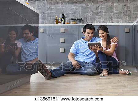 Stock Image - Full length of young couple looking at digital tablet in kitchen. Fotosearch