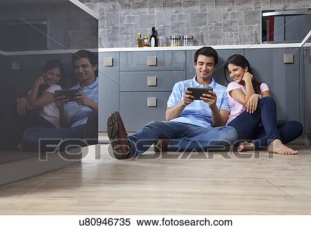 Stock Photography - Full length of young couple sharing digital tablet in kitchen. Fotosearch