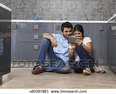 Stock Image - Full length of young couple using digital tablet in kitchen. Fotosearch