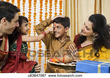 Stock Photo - Girl putting a tikka on her brothers forehead . Fotosearch