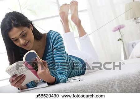 Stock Image - Girl reading a book in bed . Fotosearch