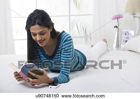 Stock Image - Girl reading a book in bed . Fotosearch