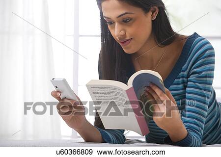 Stock Photo - Girl reading an sms while holding a book . Fotosearch