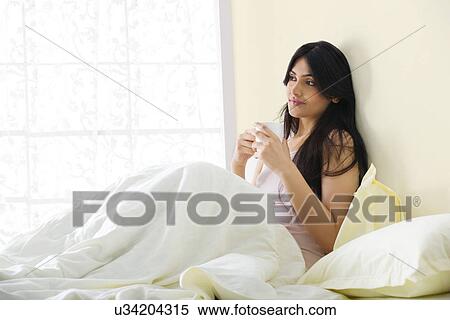Stock Photography - Girl sitting in bed with a cup of coffee . Fotosearch