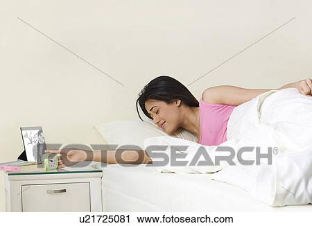 Stock Image - Girl switching off her alarm clock . Fotosearch