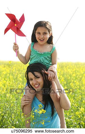 Stock Photography - Girl with a pinwheel sitting on her mothers shoulders . Fotosearch