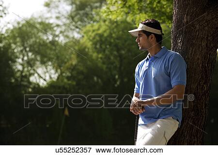 Stock Photo - Golfer leaning against a tree . Fotosearch