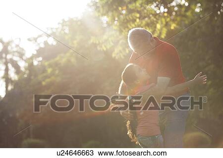 Stock Image - Grandfather and granddaughter hugging in a park. Fotosearch