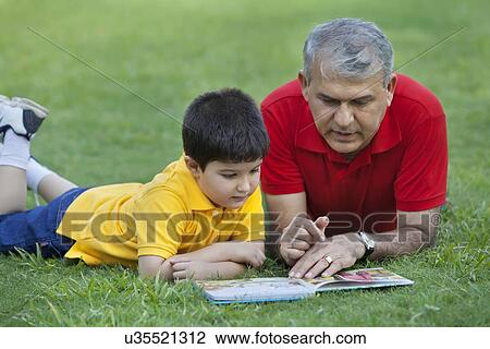 Stock Image - Grandfather and grandson reading a book in a park. Fotosearch