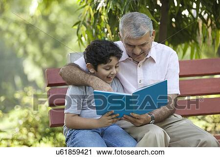 Stock Image - Grandfather and grandson reading a book in a park. Fotosearch