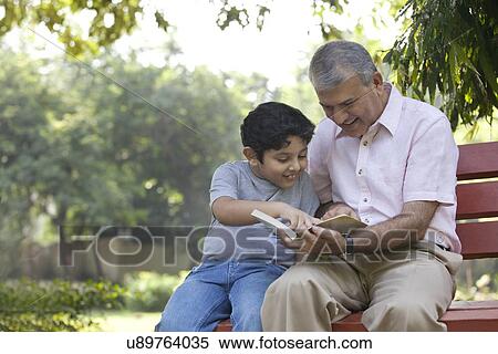 Grandfather and grandson reading a book in a park View Large Photo Image Stock Photography - Grandfather and grandson reading a book in a park. Fotosearch
