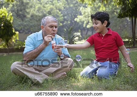 Stock Image - Grandfather blowing bubbles for grandson. Fotosearch