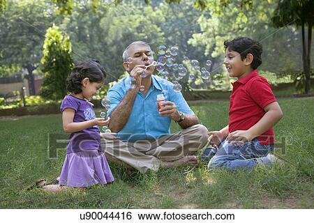 Stock Photograph - Grandfather blowing bubbles for grandchildren. Fotosearch
