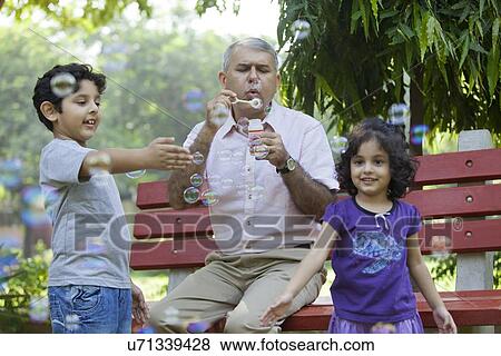 Grandfather blowing bubbles with grandchildren in park View Large Photo Image Stock Photo - Grandfather blowing bubbles with grandchildren in park. Fotosearch