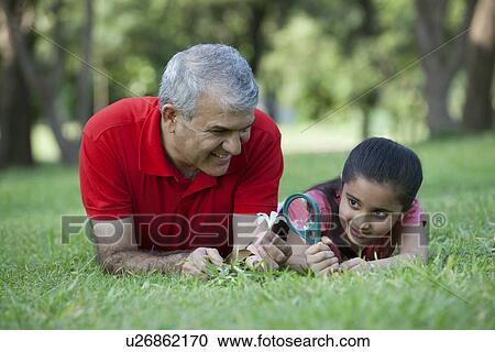 Stock Image - Grandfather holding flower while granddaughter looks through magnifying glass. Fotosearch