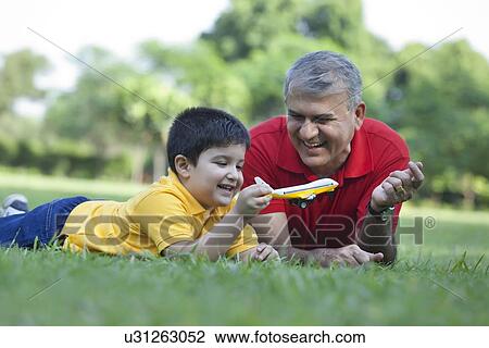 Stock Image - Grandfather watching grandson play with toy aeroplane. Fotosearch