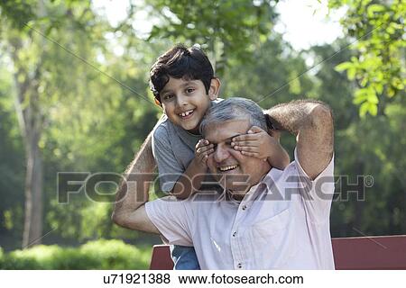 Stock Photo - Grandson covering grandfathers eyes. Fotosearch
