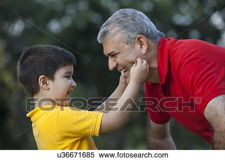 Stock Photography - Grandson squeezing his grandfathers cheeks. Fotosearch
