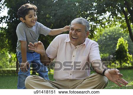 Stock Image - Grandson tickling grandfather in ear. Fotosearch