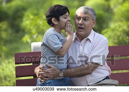 Stock Photo - Grandson whispering in grandfathers ear. Fotosearch