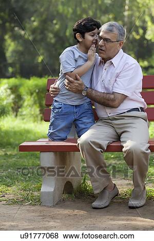 Stock Photo - Grandson whispering in grandfathers ear. Fotosearch