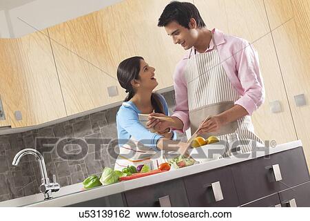 Stock Image - Happy couple preparing salad in kitchen. Fotosearch