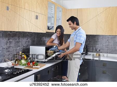 Happy young couple preparing meal together in kitchen View Large Photo Image Stock Image - Happy young couple preparing meal together in kitchen. Fotosearch