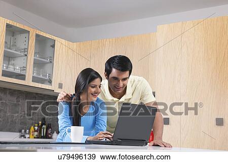 Happy young couple using laptop in kitchen View Large Photo Image Stock Photo - Happy young couple using laptop in kitchen. Fotosearch