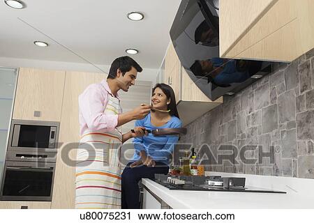 Stock Image - Indian couple cooking food in kitchen. Fotosearch