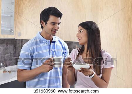 Stock Image - Indian couple having pasta and coffee in kitchen. Fotosearch