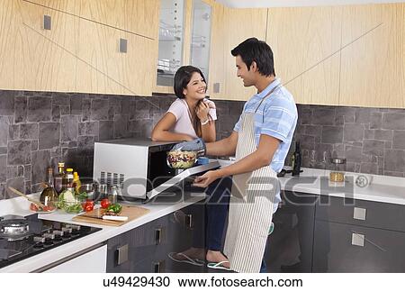 Stock Image - Indian couple preparing food together in kitchen. Fotosearch
