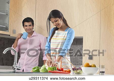Man drinking coffee while woman cutting vegetables in kitchen View Large Photo Image Picture - Man drinking coffee while woman cutting vegetables in kitchen. Fotosearch