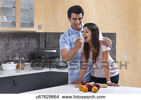 Picture - Man feeding apple to woman in kitchen. Fotosearch