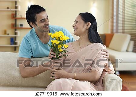 Stock Photography - Man giving mother bunch of flowers at home . Fotosearch