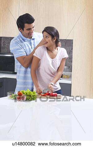 Stock Image - Man giving necklace to surprised woman in kitchen. Fotosearch