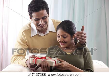 Stock Photo - Man surprising a woman with a gift on Valentines Day. Fotosearch