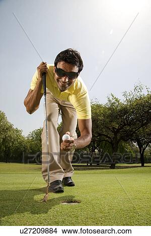 Picture - Man taking a golf ball out of a hole . Fotosearch