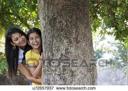 Stock Photo - Mother and daughter hiding behind a tree . Fotosearch