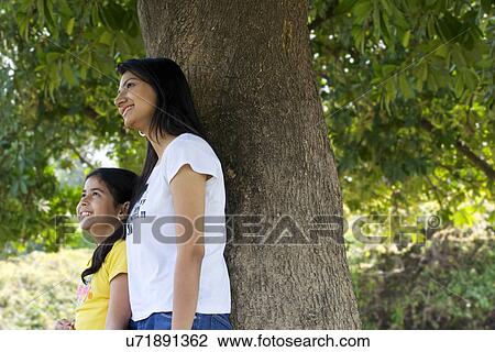 Stock Image - Mother and daughter leaning against a tree . Fotosearch